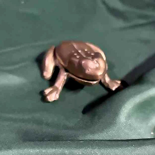 Bronze frog figurine on a green textured surface