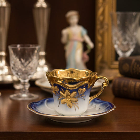 Small ornate cup and saucer with gold detailing on a green fabric background