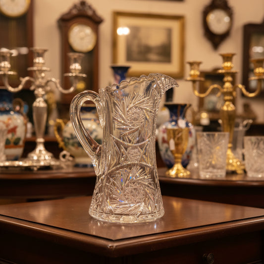 Clear glass pitcher with intricate designs on a green satin background