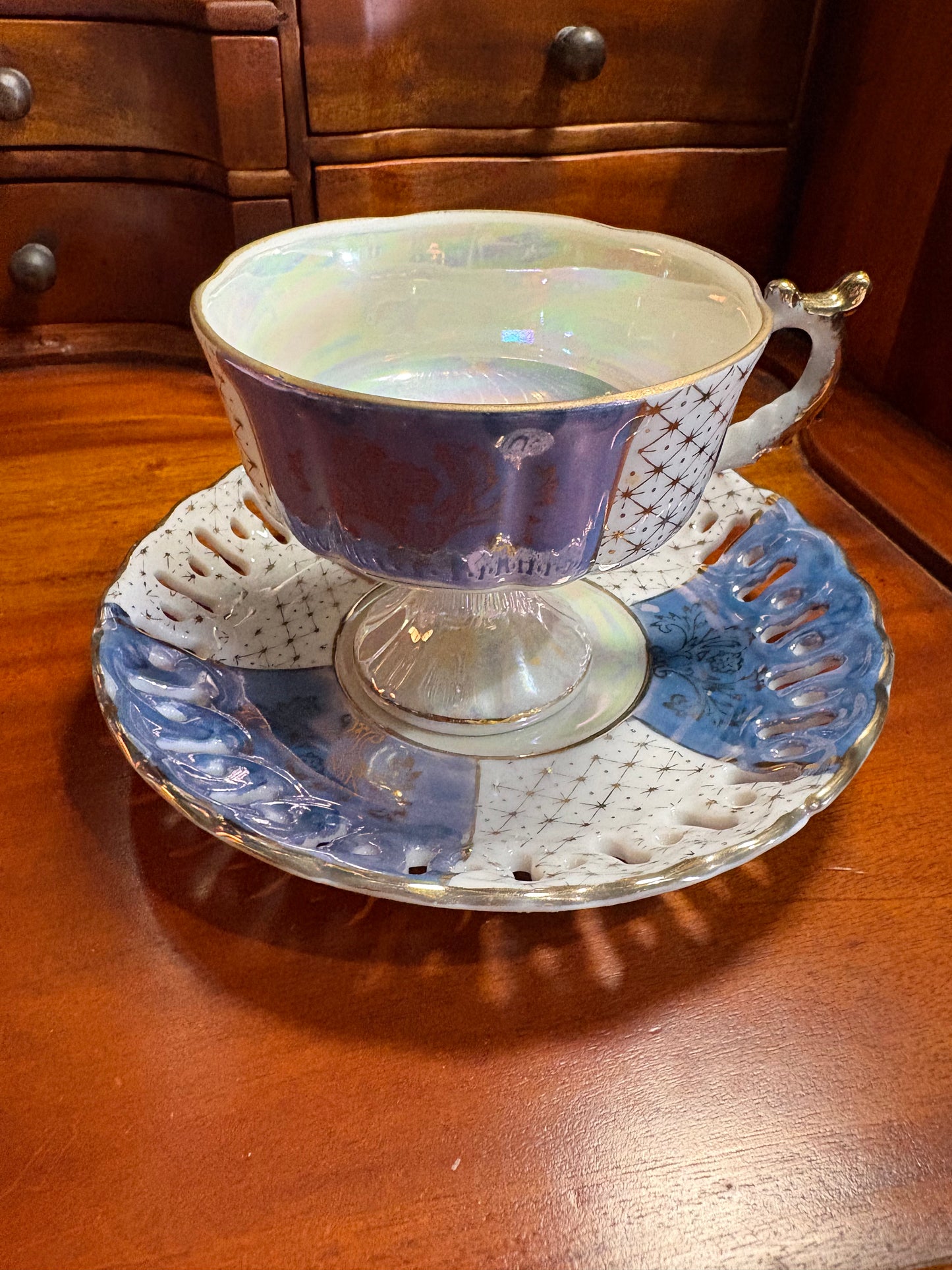 An iridescent purple and white porcelain teacup with a matching saucer, displayed on a wooden table.