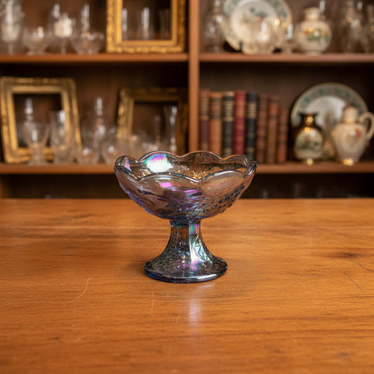 An iridescent glass pedestal bowl with a scalloped rim, resting on a draped gray fabric background.