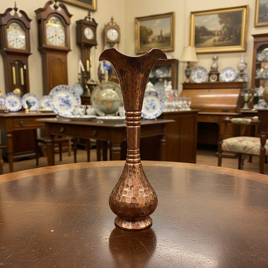 A small copper-colored glass vase with a flared, wavy rim and a textured, faceted body, standing on a dark gray fabric backdrop.