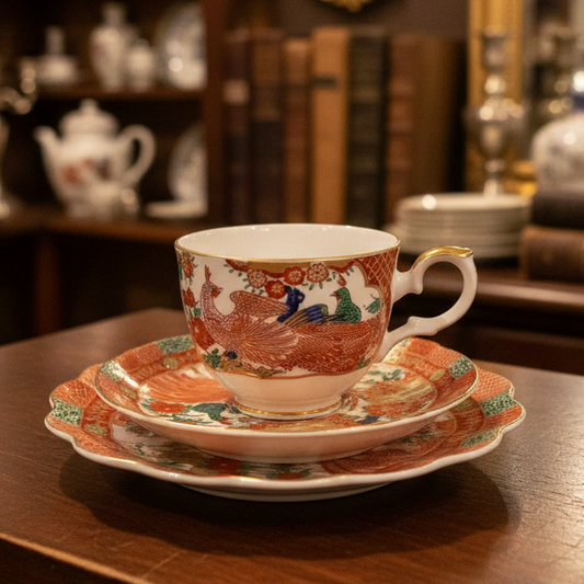 A vintage Japanese-style ceramic teacup and saucer set with a vibrant red and multicolor floral pattern, displayed on a draped dark green fabric background.