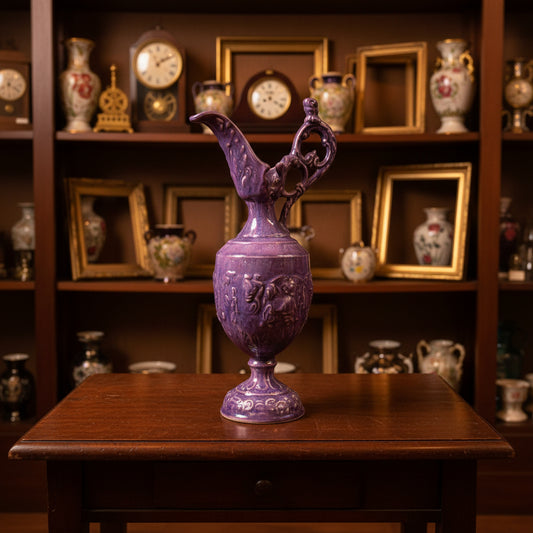 A vintage-style pink glass pitcher with a bulbous body, flared base, and curved spout, photographed against a draped gray fabric backdrop.