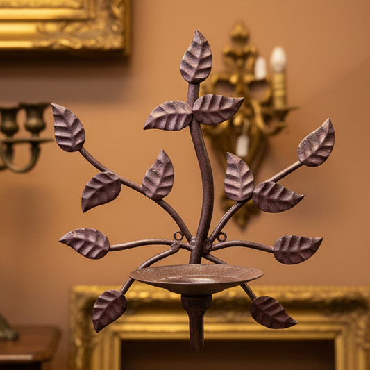 A small decorative metal wall piece shaped like a leafy branch with a circular base, shown against a draped gray fabric backdrop.