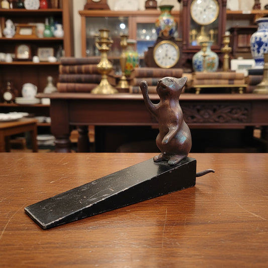 A small metallic pink cat figurine standing on a black rectangular base, photographed against draped gray fabric.