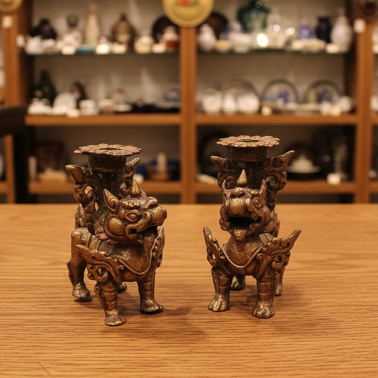 Two small ornate figurines with a metallic bronze and purple patina finish, displayed side by side on a draped dark gray fabric background.